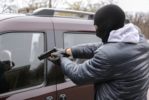 Masked person pointing gun at vehicles window.