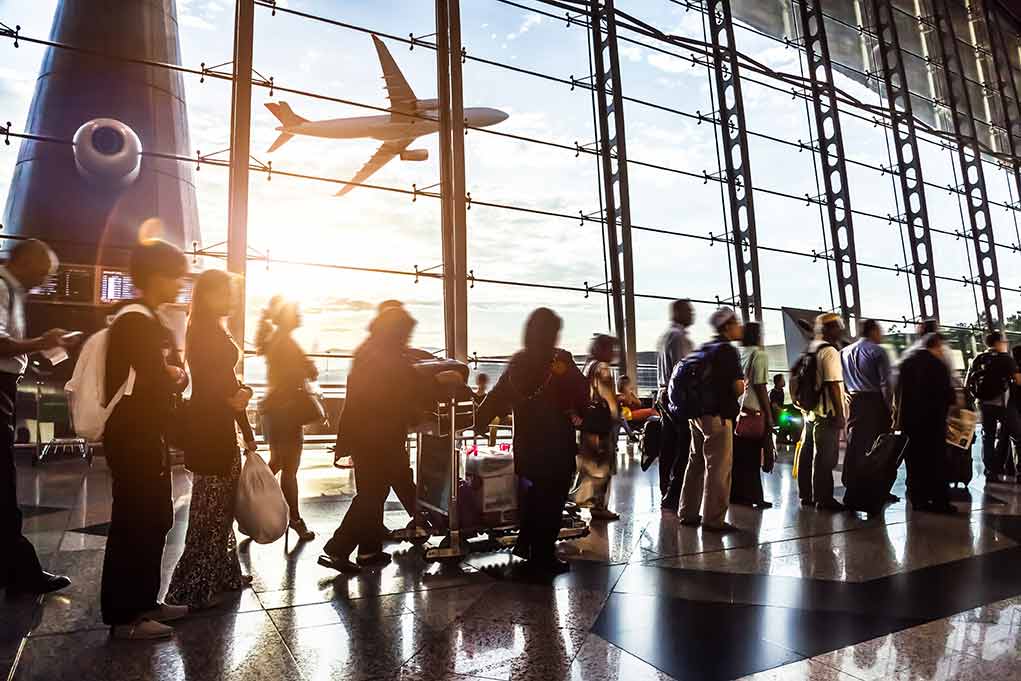 People queuing inside airport terminal with airplane flying outside.
