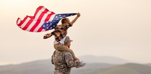 Child on soldiers shoulders holding American flag.