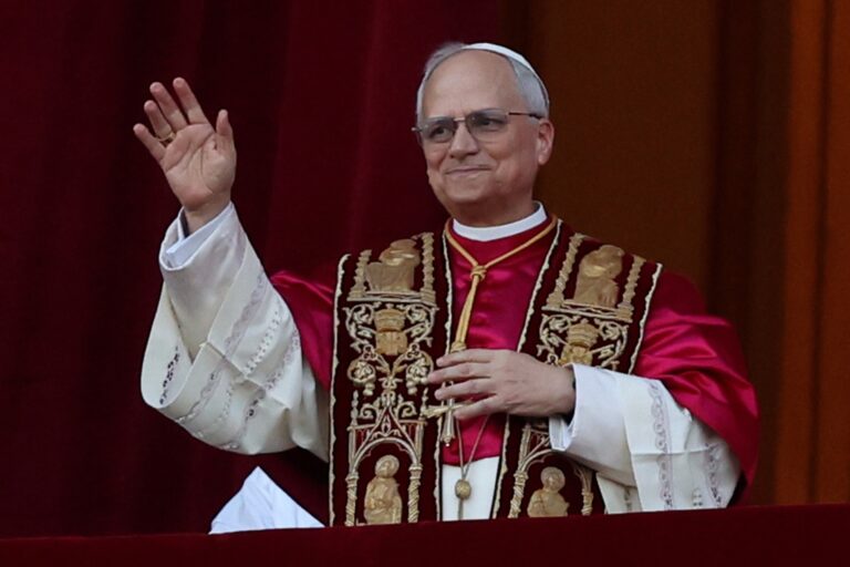 Cleric in red and white robes waving outdoors