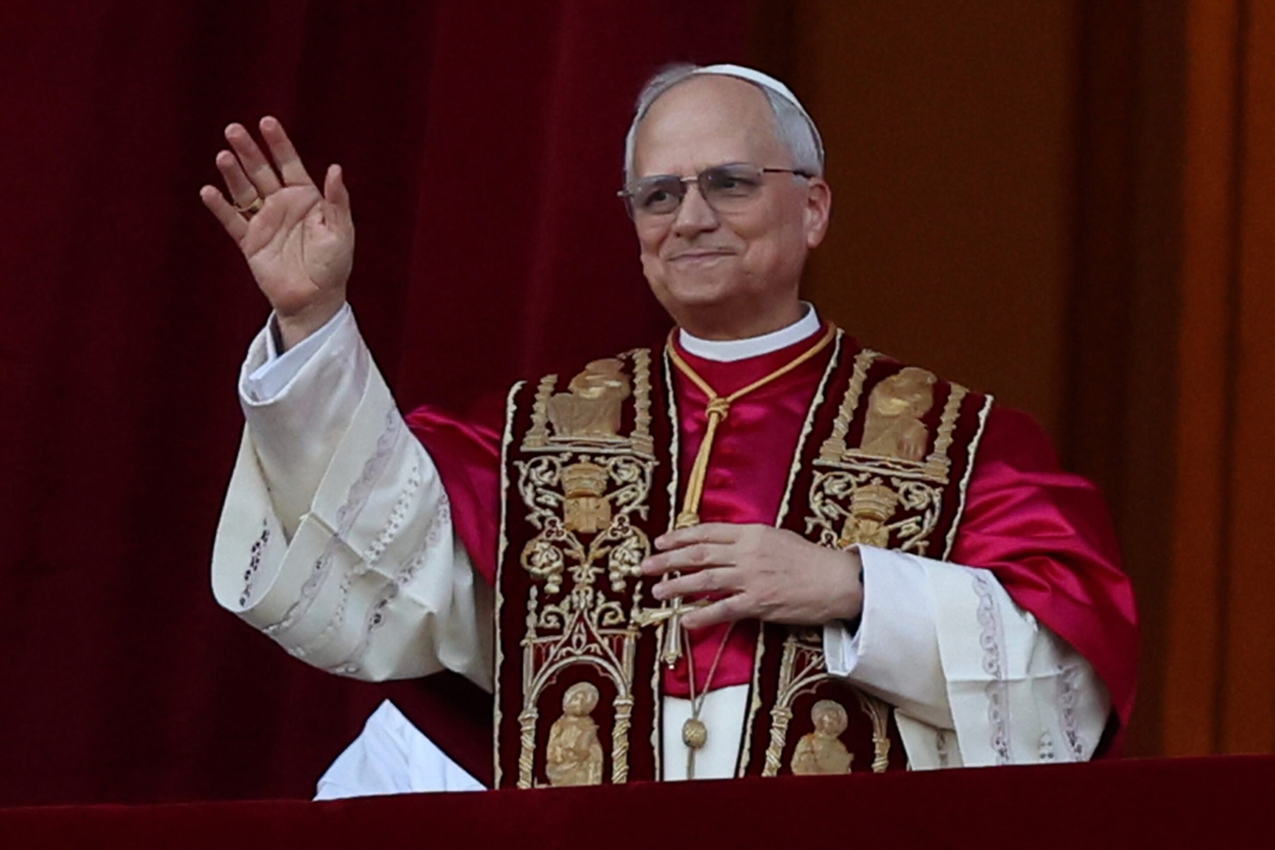 Cleric in red and white robes waving outdoors