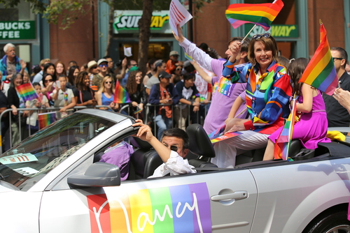 People in rainbow car at pride parade, waving flags.
