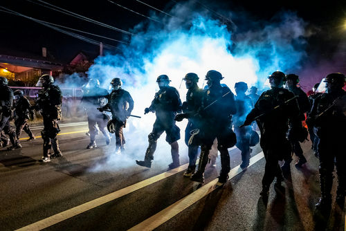 Police officers march through smoke during a nighttime protest.