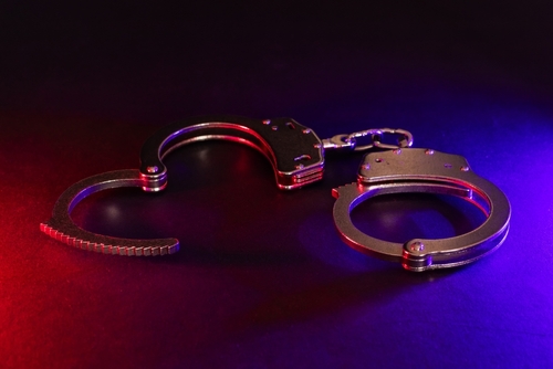 A pair of metallic handcuffs on a dark background with red and blue lighting