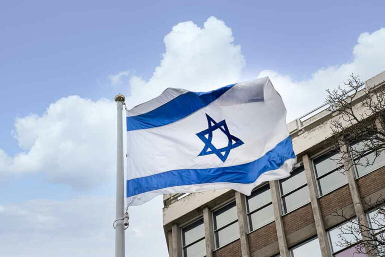 Israeli flag waving near a building with windows.