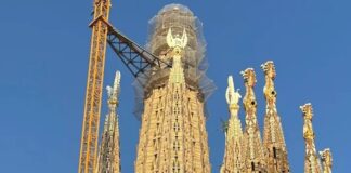 Construction view of the Sagrada Familia with cranes and intricate towers against a blue sky