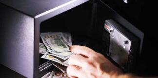 Hand placing cash into open safe.