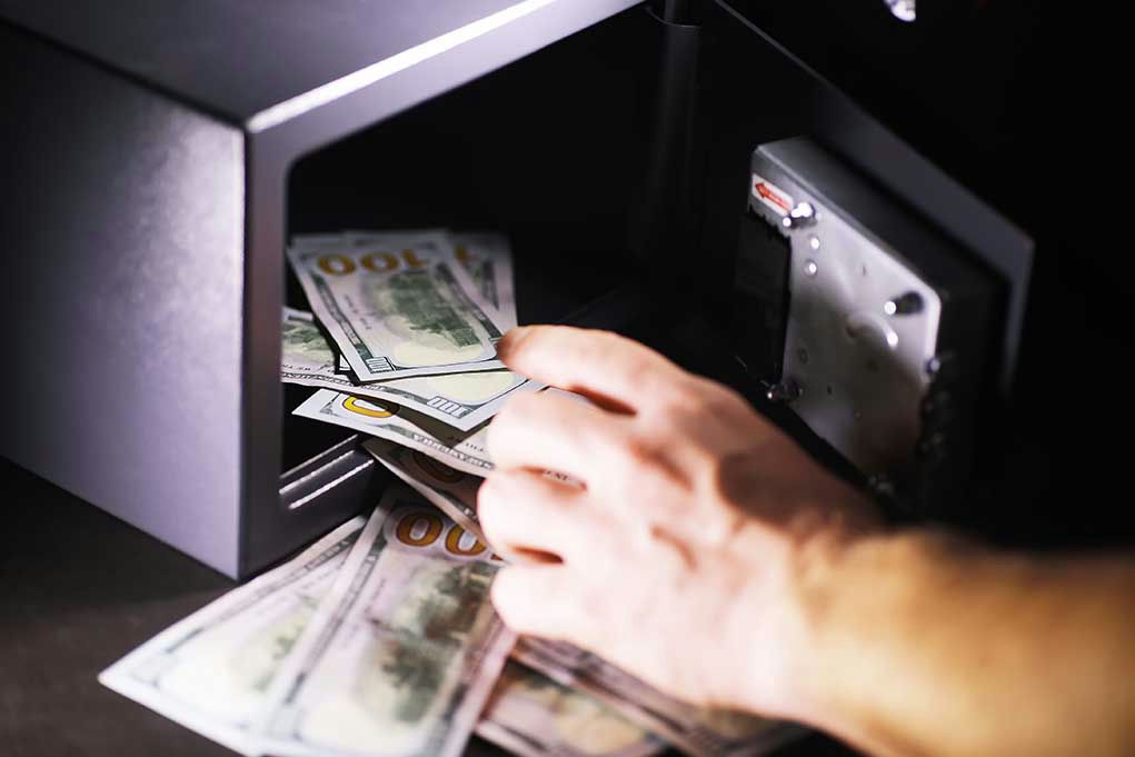 Hand placing cash into open safe.